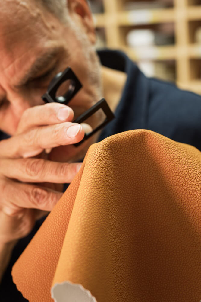 Man looking at tan fabric texture with a magnifying loupe.