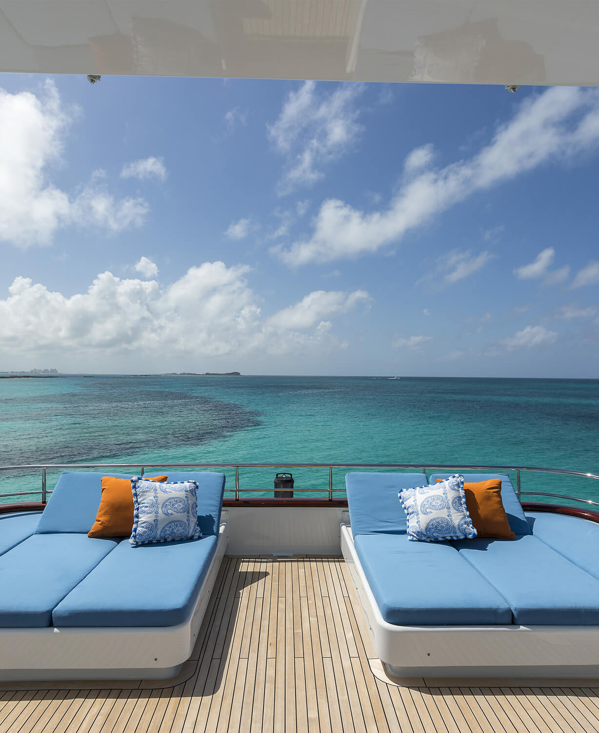 Luxury boat deck with blue cushioned lounge-seating on the water with blue sky and clouds in background.