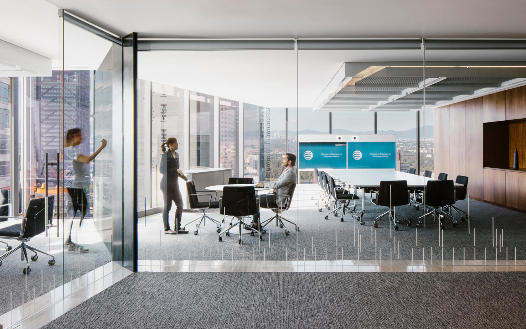 Modern office conference room with big glass doors, conference tables, and chairs, and a city view outside.