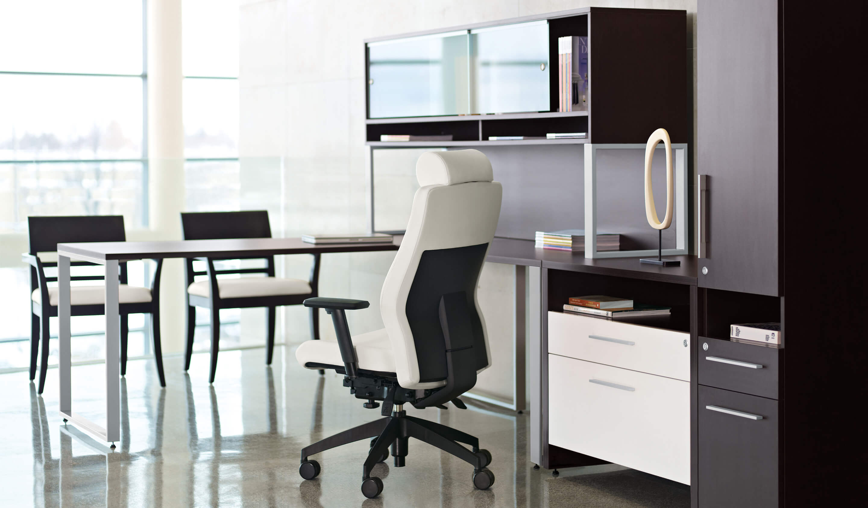 Modern office with black and white cubicle drawers, white fabric office chair and two meetings chairs.