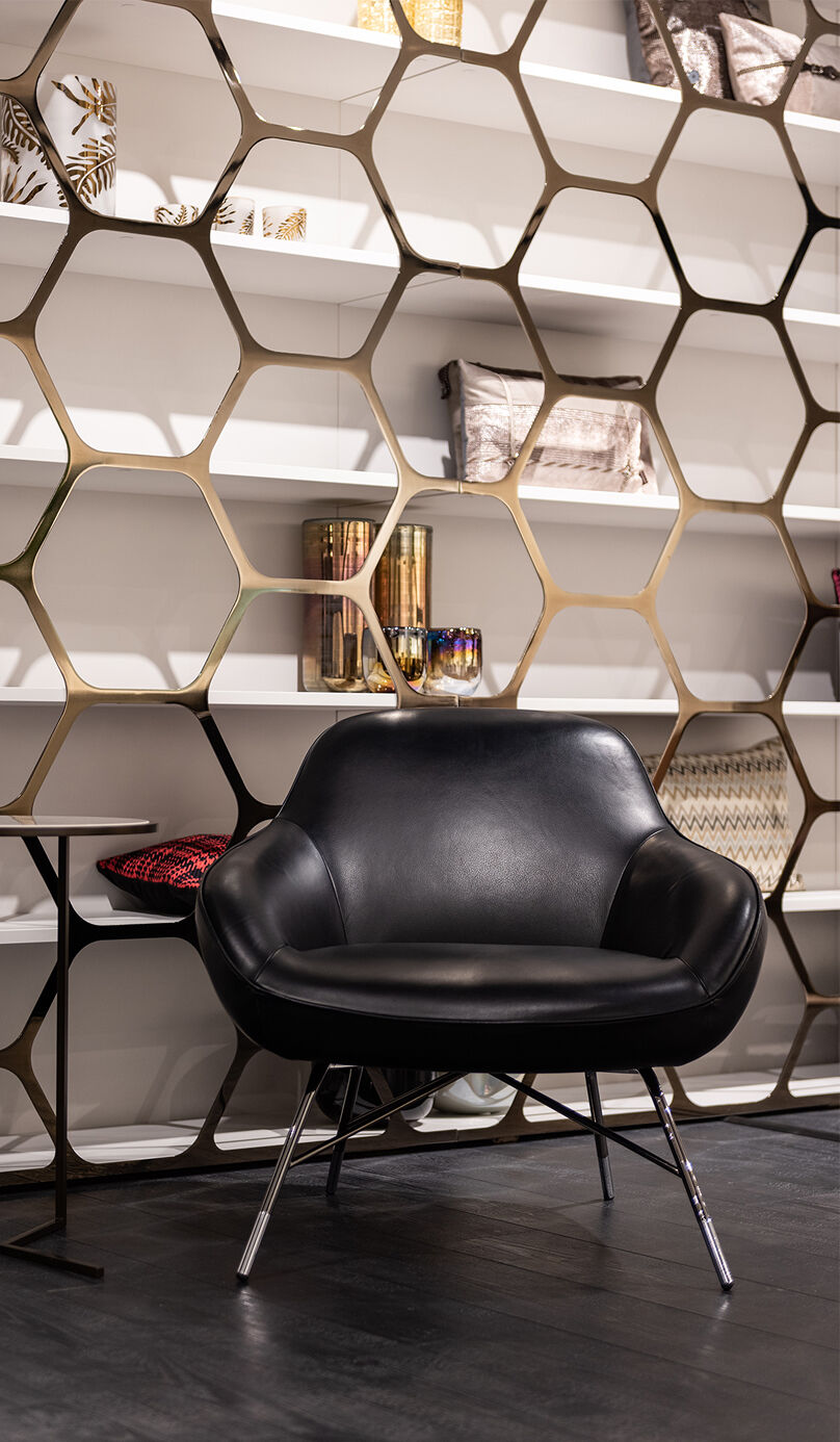 Modern black leather chair in front of decorative gold, hexagonal shelving.