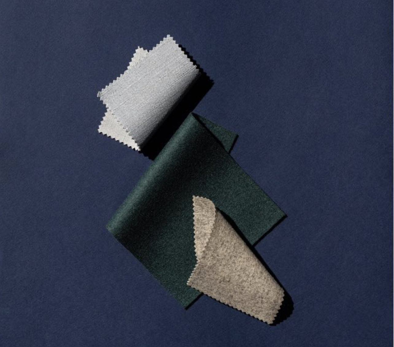 Gray fabric, green fabric, and tan fabric folded on a dark blue background.